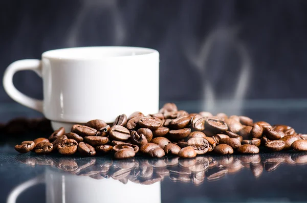 黒い背景にコーヒー豆。生のコーヒー豆粒状の製品。熱い飲み物クローズアップ。収穫。自然な背景。エネルギー。ガラスの反射。コーヒーフォーム付きコーヒーのホワイトカップ — ストック写真