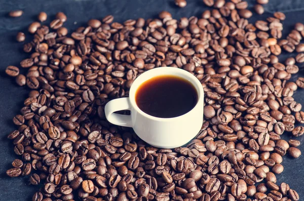 黒い背景にコーヒー豆。生のコーヒー豆粒状の製品。熱い飲み物クローズアップ。収穫。自然な背景。エネルギー。ガラスの反射。コーヒーフォーム付きコーヒーのホワイトカップ — ストック写真