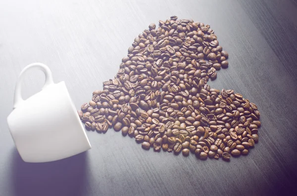 Corazón consisten en granos de café. Café frijoles tostados en una forma como un corazón y taza de café. Fondo rústico. Energía . — Foto de Stock