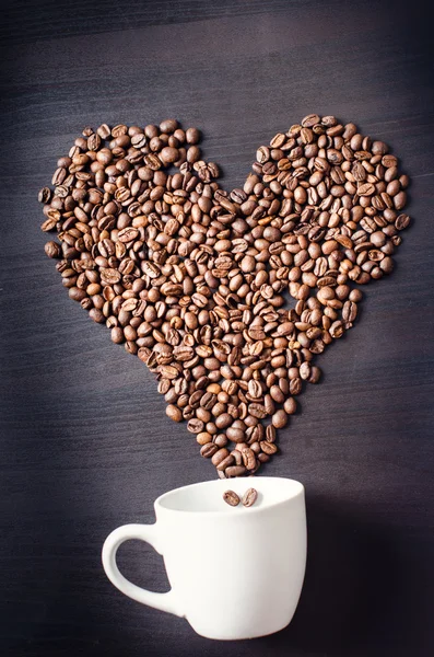 心臓はコーヒー豆から成っている。ハートとコーヒーカップのような形のコーヒーロースト豆。素朴な背景。エネルギー. — ストック写真
