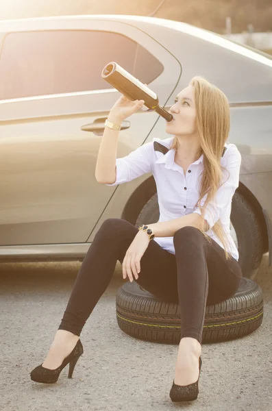 Mujer borracha sentada en un volante en coche. Una mujer bebe alcohol. Jovencita sexy. Repara un auto. Accidente de coche . — Foto de Stock