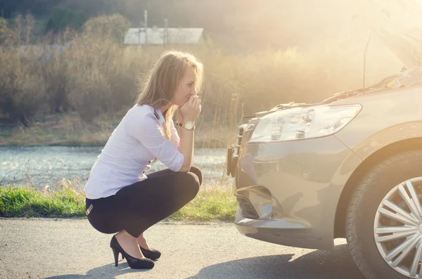 Mujer agachada en la carretera junto a un triángulo de advertencia rojo. Triste persona. Coche dañado. Fondo natural. Accidente de coche . — Foto de Stock