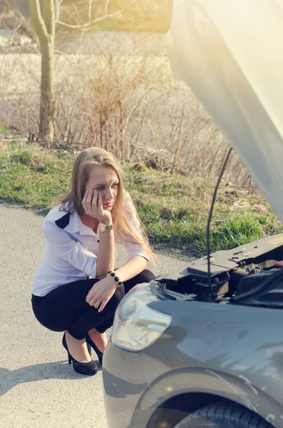 Mujer agachada en la carretera junto a un triángulo de advertencia rojo. Triste persona. Coche dañado. Fondo natural. Accidente de coche . — Foto de Stock