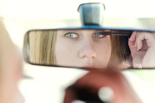 Una mujer maquillándose en un coche. Una joven guapa mirándose en el espejo. Situación peligrosa . — Foto de Stock