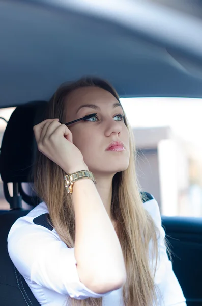 Una mujer maquillándose en un coche. Una joven guapa mirándose en el espejo. Situación peligrosa . — Foto de Stock