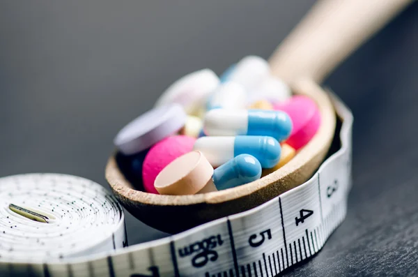 Pharmacy background on a black table with measuring tape. Tablets on a wooden spoon. Pills. Medicine and healthy. Close up of capsules. Differend kind of pills — Stockfoto
