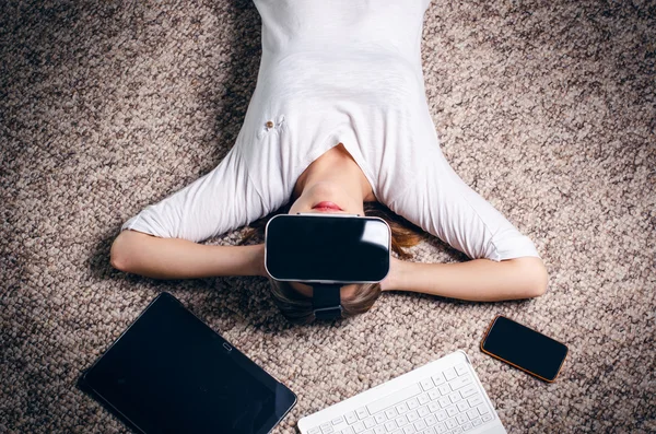 Woman with virtual reality goggles lie on a carpet. Studio. Woman show a gesture.