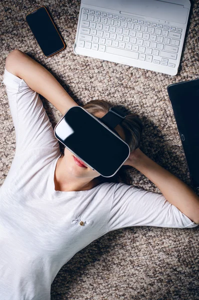 Woman with virtual reality goggles lie on a carpet. Studio. Woman show a gesture.