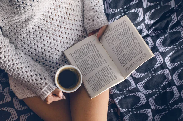 Ayrıntı seksi genç kadın. Kadın bir fincan kahve tutmak ve bir kitap okuyun. Bir battaniye üzerinde oturuyor... Çıplak bacaklar. Ev atmosfer. 