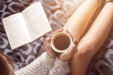     Seksi genç kadın ve güneş ışığı detayını. Kadın bir fincan kahve tutmak ve bir kitap okuyun. Bir battaniye üzerinde oturuyor... Çıplak bacaklar. Ev atmosfer. 