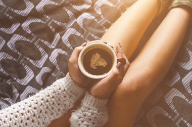      Seksi genç kadın ve güneş ışığı detayını. Kadın bir fincan kahve tutmak ve bir kitap okuyun. Bir battaniye üzerinde oturuyor... Çıplak bacaklar. Ev atmosfer. 