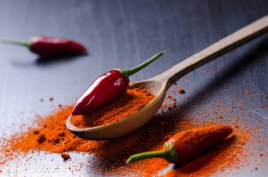 Soğuk kırmızı biber ile baharatlı, siyah ahşap bir masaya. Üzerinde bir tahta kaşık biber. Sebze. Sıcak yemek kavramı. 