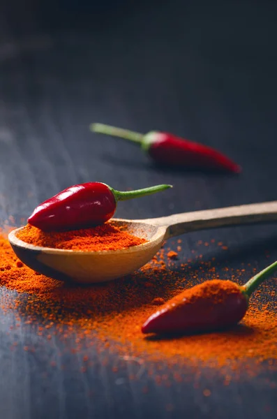 Rode kille paprika's op een houten, zwarte tafel met pittige. Spaanse peper op een houten lepel. Plantaardige. Concept van warm voedsel. — Stockfoto