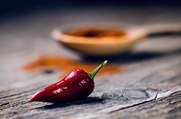 Peperoni rossi piccanti su un cucchiaio di legno. Verdura su un tavolo di legno scuro. Concetto di cibo caldo . — Foto Stock