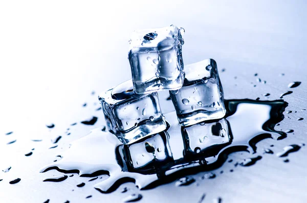 Cubes glacés fondus sur une table bleue avec réflexion. De l'eau. Fonte de la glace . — Photo