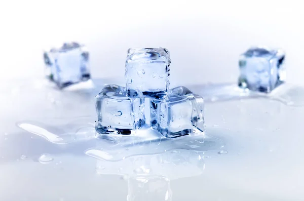 Iced isbitar som smälter på ett vitt bord med reflektion. Vatten. Smältning av isen. — Stockfoto