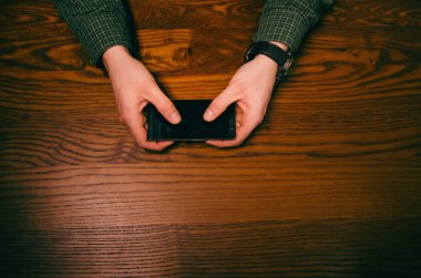  Adam el dokunmak ahşap bir masa üstünde hareket eden telefon ekranında. İş durumu.