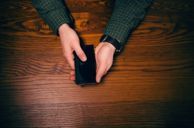  Adam el dokunmak ahşap bir masa üstünde hareket eden telefon ekranında. İş durumu.