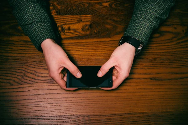 Man hand touch on a screen of mobile phone on a wooden table. Business situation.