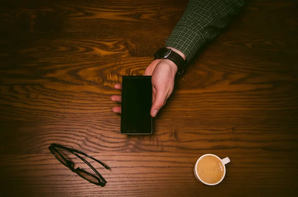 Man hand touch on a screen of mobile phone on a wooden table. Business situation