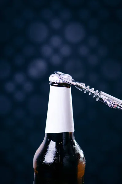 Glass bottle of beer and opener on a dark background. Hand opening a bottle. Alcohol and drinks concept. Royalty Free Stock Photos