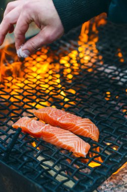 Bir ızgarada Somon ızgara biftek. Yangın alev ızgara. Restoran ve Bahçe mutfak. Bahçe partisi. Sağlıklı yemek. Çiğ et ve güneş ışığı. Adam elini tutun ve tuz et.