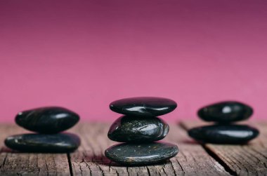 Siyah taş tedavi. Spa ve sağlıklı yaşam konsepti. Bir ahşap masa ve pembe bir arka plan üzerinde bir pembe çiçek. Güzel çiçekler. Bayram tebrik kartı. Pastel renk... Bahar.