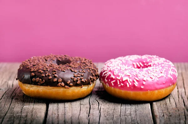 Donut mit Streusel auf einem Holztisch und rosa Hintergrund. zwei Arten von Donuts. Kuchen und Süßes. Lebensmitteldetails. Nahaufnahme. Pastellfarbe — Stockfoto