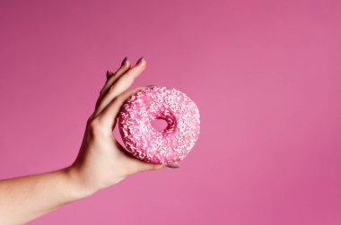 El ile sprinkles bir ahşap masa ve pembe bir arka plan üzerinde renkli donut tutarak. Çörek iki tür. Pasta ve tatlı. Gıda ayrıntı. Yakın çekim. Pastel renk