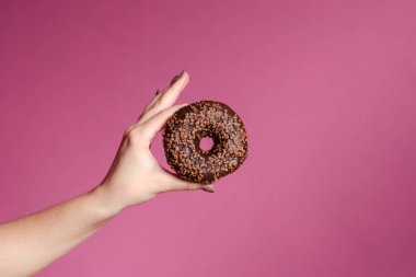 El ile sprinkles bir ahşap masa ve pembe bir arka plan üzerinde renkli donut tutarak. Çörek iki tür. Pasta ve tatlı. Gıda ayrıntı. Yakın çekim. Pastel renk