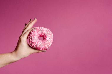 El ile sprinkles bir ahşap masa ve pembe bir arka plan üzerinde renkli donut tutarak. Çörek iki tür. Pasta ve tatlı. Gıda ayrıntı. Yakın çekim. Pastel renk