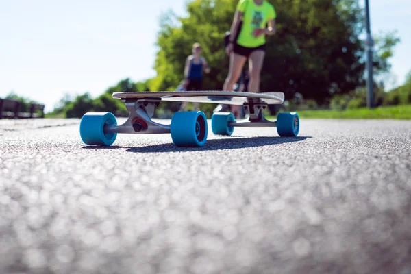 Longboard on the road in sunny weather. People around skateboard. Pathway in a park. Urban scene. — Stock Photo, Image