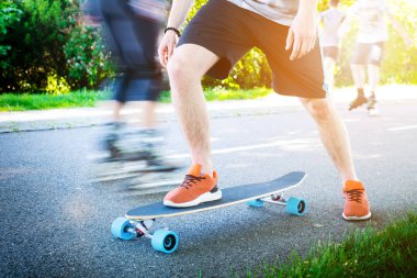 Genç adam bir longboard üzerinde sürme. Güneşli havalarda yolda longboard. Kaykay etrafında insanlar. Yolu bir parkta. Kentsel sahne.