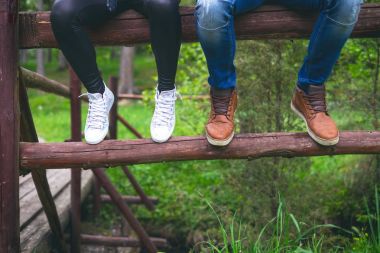 Cep telefonları tutarak ve gülen genç, modern çift. Modern ilişkiler kavramı. Ormandaki bir odun oturan hipster insanların yakın çekim.