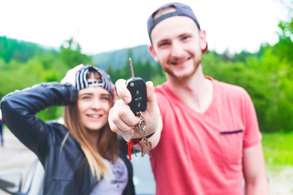 Hermosas parejas jóvenes compran un coche nuevo y muestran una llave. Concepto de transporte. Jóvenes felices . — Foto de Stock