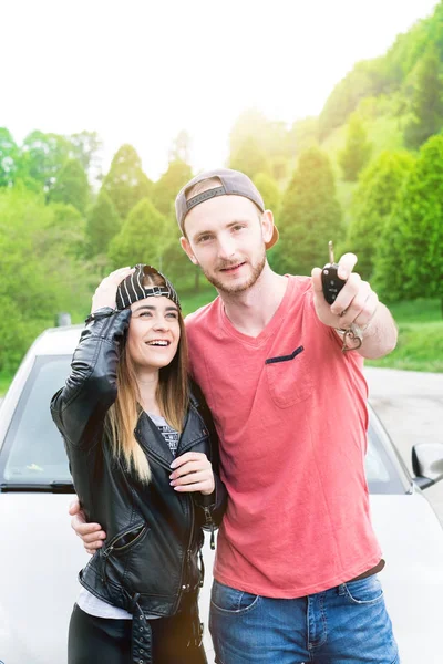 Hermosas parejas jóvenes compran un coche nuevo y muestran una llave. Concepto de transporte. Jóvenes felices . — Foto de Stock