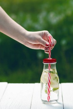 Kadın el ev yapımı aromalı su ile limon, limon ve mentha Bahçe beyaz bir tablo yenileme devam et. Yaz saati. İçecekler.