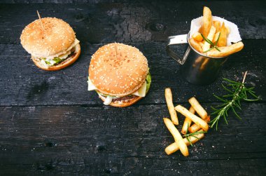 Yanmış, siyah ahşap bir masada patates kızartmalı hamburger. Fast food yemeği. Ev yapımı hamburger sığır eti, marul, domates, teneke, sos, peynir ve baharatlardan oluşur. Eski