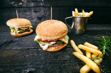 Yanmış, siyah ahşap bir masada patates kızartmalı hamburger. Fast food yemeği. Ev yapımı hamburger sığır eti, marul, domates, teneke, sos, peynir ve baharatlardan oluşur. Eski