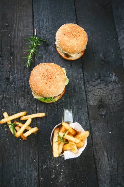 Yanmış, siyah ahşap bir masada patates kızartmalı hamburger. Fast food yemeği. Ev yapımı hamburger sığır eti, marul, domates, teneke, sos, peynir ve baharatlardan oluşur. Eski