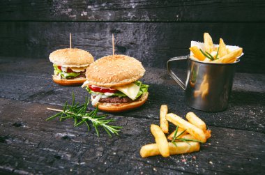 Yanmış, siyah ahşap bir masada patates kızartmalı hamburger. Fast food yemeği. Ev yapımı hamburger sığır eti, marul, domates, teneke, sos, peynir ve baharatlardan oluşur. Eski