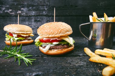 Yanmış, siyah ahşap bir masada patates kızartmalı hamburger. Fast food yemeği. Ev yapımı hamburger sığır eti, marul, domates, teneke, sos, peynir ve baharatlardan oluşur. Eski