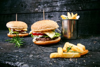 Yanmış, siyah ahşap bir masada patates kızartmalı hamburger. Fast food yemeği. Ev yapımı hamburger sığır eti, marul, domates, teneke, sos, peynir ve baharatlardan oluşur. Eski