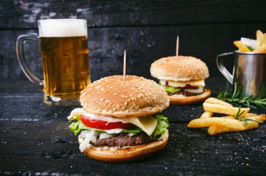 Yanmış, siyah ahşap bir masada patates kızartmalı hamburger. Fast food yemeği. Ev yapımı hamburger sığır eti, marul, domates, teneke, sos, peynir ve baharatlardan oluşur. Eski