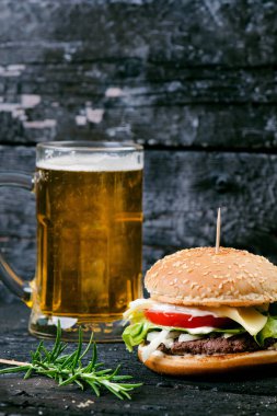 Yanmış, siyah ahşap bir masada patates kızartmalı hamburger. Fast food yemeği. Ev yapımı hamburger sığır eti, marul, domates, teneke, sos, peynir ve baharatlardan oluşur. Eski