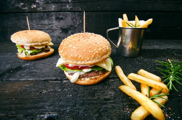 Yanmış, siyah ahşap bir masada patates kızartmalı hamburger. Fast food yemeği. Ev yapımı hamburger sığır eti, marul, domates, teneke, sos, peynir ve baharatlardan oluşur. Eski