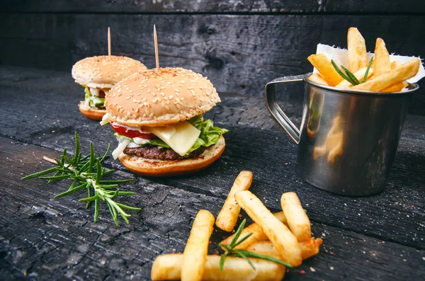 Yanmış, siyah ahşap bir masada patates kızartmalı hamburger. Fast food yemeği. Ev yapımı hamburger sığır eti, marul, domates, teneke, sos, peynir ve baharatlardan oluşur. Eski