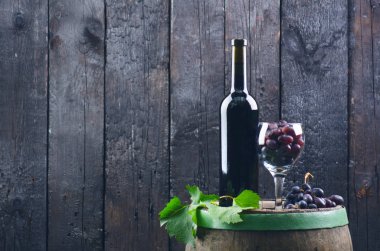 Adam kırmızı şarap dolduruyor. Tahta fıçıda şarap. Yanmış, siyah ahşap arka plan. Eski model. Bir metin için kopyalanmış boşluk. Üzüm ve yeşil üzüm. 