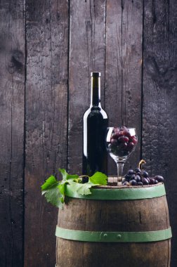 Adam kırmızı şarap dolduruyor. Tahta fıçıda şarap. Yanmış, siyah ahşap arka plan. Eski model. Bir metin için kopyalanmış boşluk. Üzüm ve yeşil üzüm. 