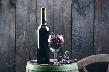 Adam kırmızı şarap dolduruyor. Tahta fıçıda şarap. Yanmış, siyah ahşap arka plan. Eski model. Bir metin için kopyalanmış boşluk. Üzüm ve yeşil üzüm. 